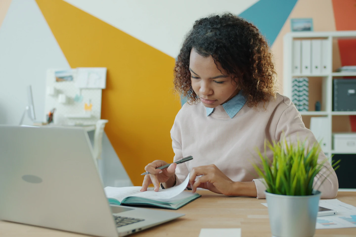 A person reviewing notes and a laptop at a working desk.