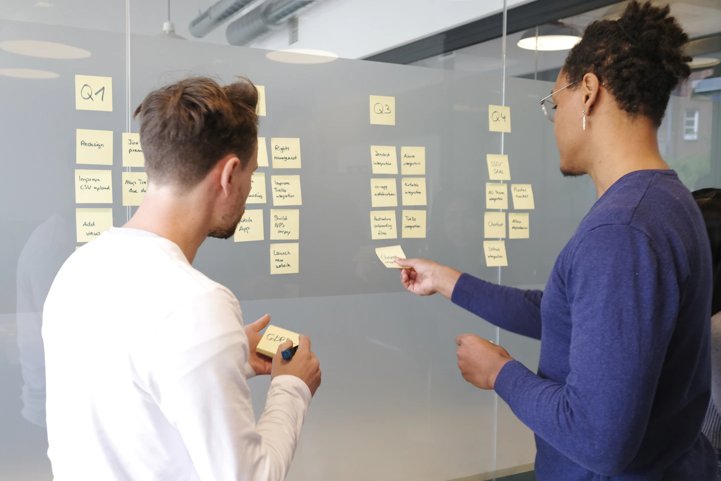 Two colleagues arranging project notes on a glass wall.