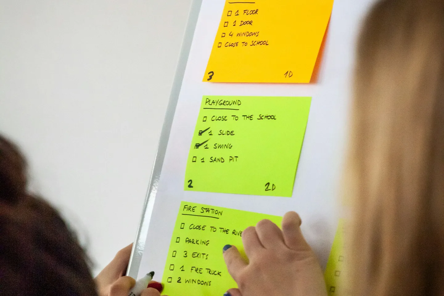 Colleagues arranging and discussing handwritten notes on a workshop board.