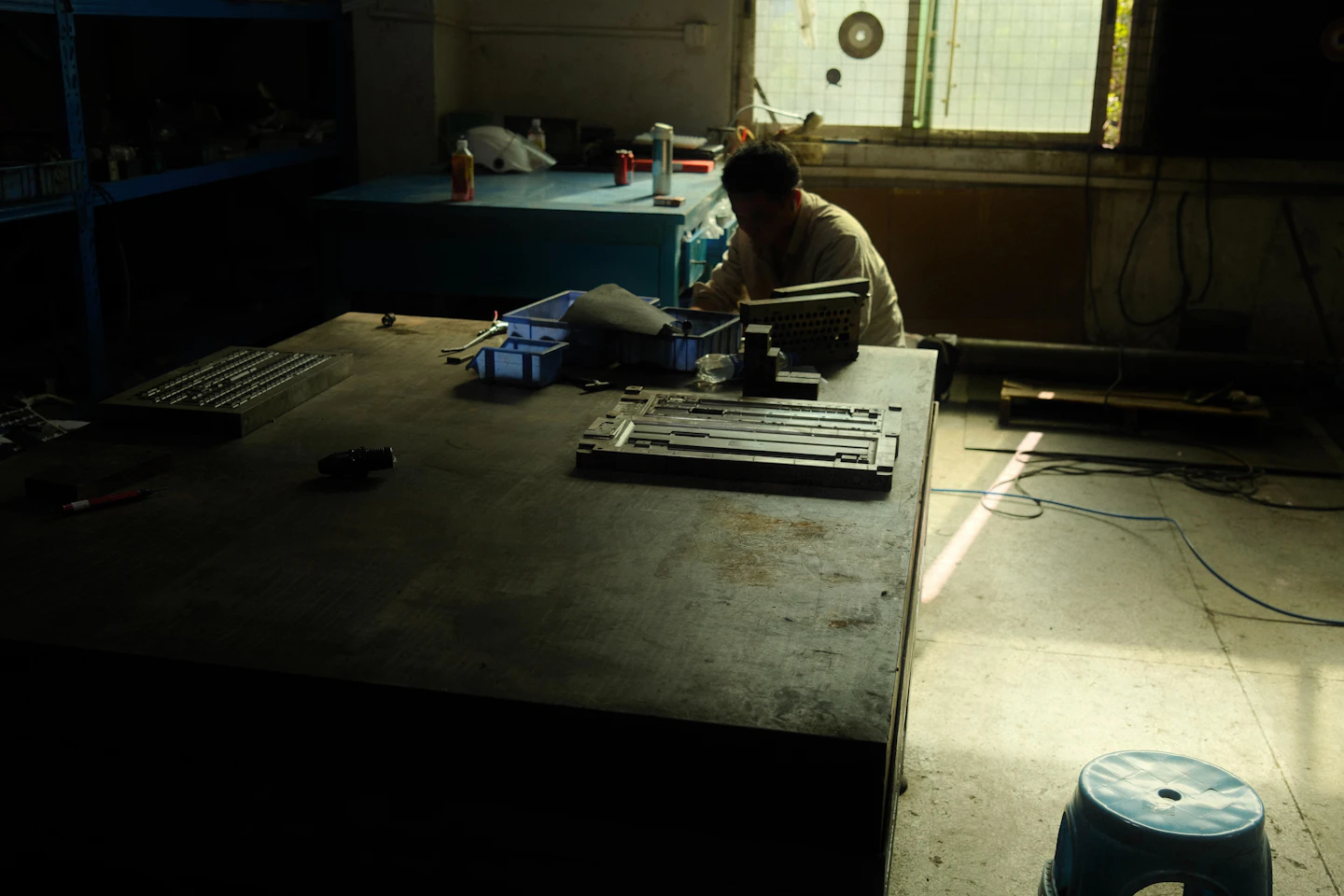 A toolmaker working at a large bench in a sunlit workshop.