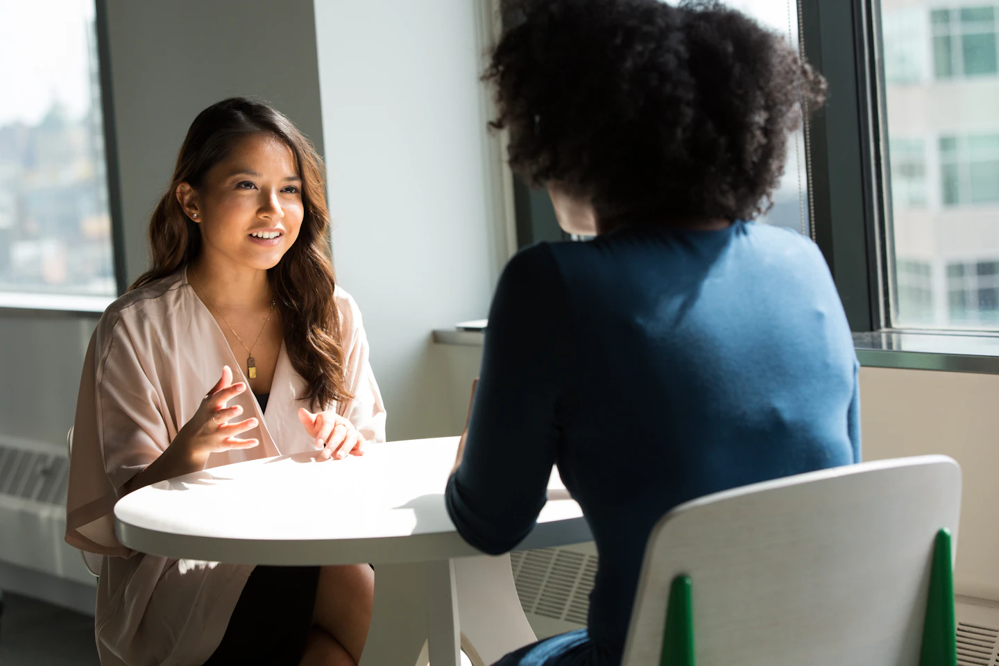 Two people in a focused conversation at a small table by a window.